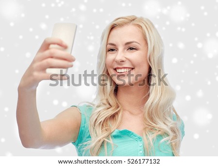 technology, winter holidays, christmas and people concept - happy smiling young woman or teenage girl taking selfie with smartphone over snow