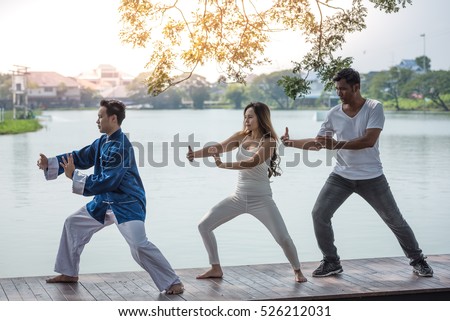 Group of young people practicing traditional Tai Chi Chuan, Tai Ji  and Qi Gong for fighting match together in the park on the lake background, traditional chinese martial arts concept. Royalty-Free Stock Photo #526212031