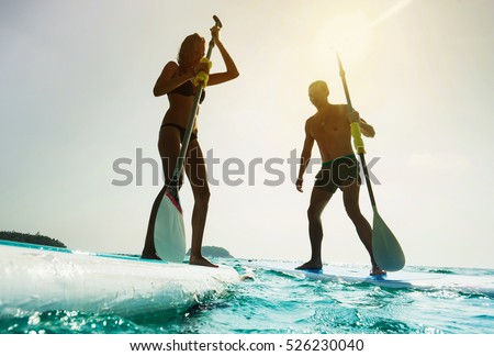 Stand up paddle board couple paddleboarding . Young caucasian couple on summer vacation. Royalty-Free Stock Photo #526230040
