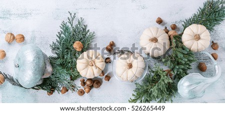 Holiday table decoration with white and silver decorative pumpkins, thuja branches, walnuts and acorns over white wooden background. Top view with space for text