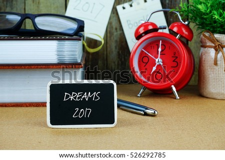 Inscription written on chalkboard. Red alarm clock, books, spectacle, notes at background.