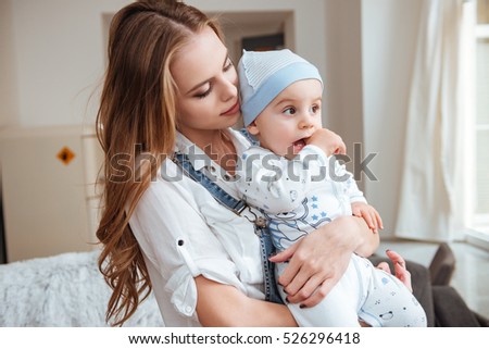Pretty young mother standing and holding her little son at home