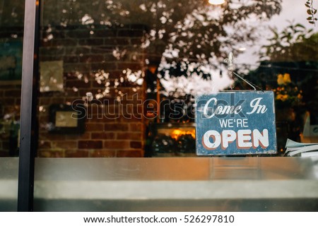 Open sign board close-up through the glass of a window at coffee shop door. Shallow depth of field. Royalty-Free Stock Photo #526297810