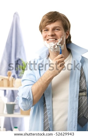 Young man shaving in the morning, smiling. Isolated on white.