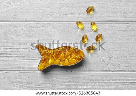 Capsules of cod liver oil arranged in a fish shape on white wooden background Royalty-Free Stock Photo #526305043