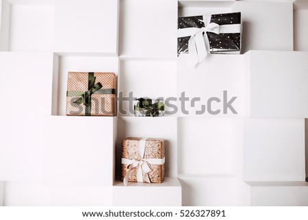 Christmas gift boxes composition. cube textured white wall background, red and green ribbons and craft, black and white paper with the fir print.