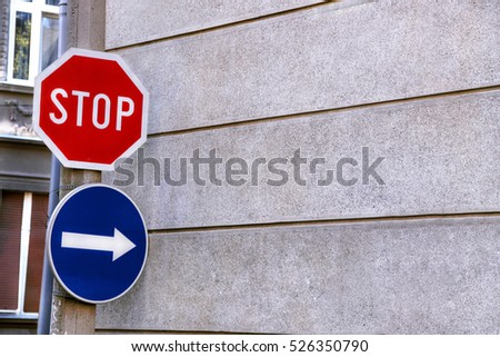 Red sign stop and blue sign arrow on the pole, next to the wall of the building