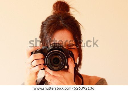Young female photographer with camera on soft background taking a picture with her new camera
