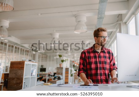 Shot of young businessman in casual clothes at modern startup business office space, working on  desktop computer. Royalty-Free Stock Photo #526395010