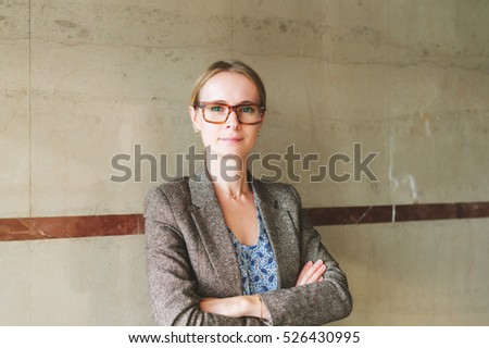 Portrait of yong 35 year old woman wearing brown eyeglasses and jacket, arms crossed