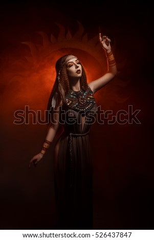 Beautiful, red-haired girl - a priestess of the sun. Dress and jewelry in ethnic style. Unusual make-up in orange and gold tones.  Fantastic photography, fashionable toning.