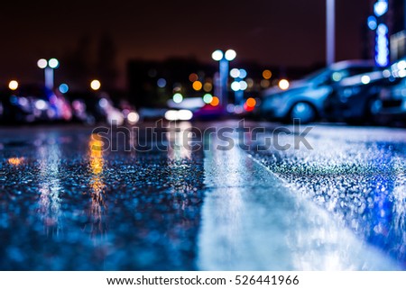 Rainy night in the parking shopping mall, rows of parked cars. Close up view from the level of the dividing line, image in the blue tones