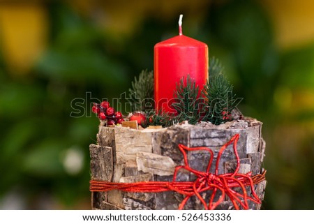 Christmas red candle on a stump decorated tree bark and berries and fir branches on a blurry background closeup