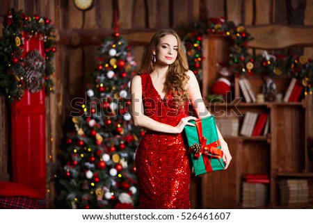 Holidays, celebration and people concept - young smiling woman in elegant red dress over christmas interior background