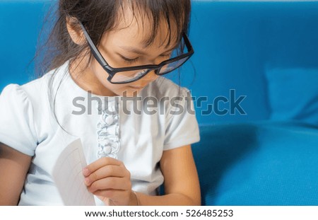 Nerdy Asian female kid is reading a book studying.