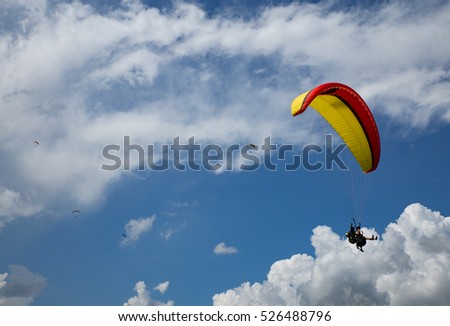 Tandem paragliders up in the blue cloudy sky.