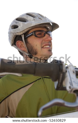 A young man wearing protective eyewear and a helmet is carrying a mountain bike. Vertical shot.