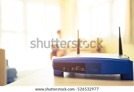 closeup of a wireless router and a young man using Laptop and notebook computers on living room at home with a window in the background