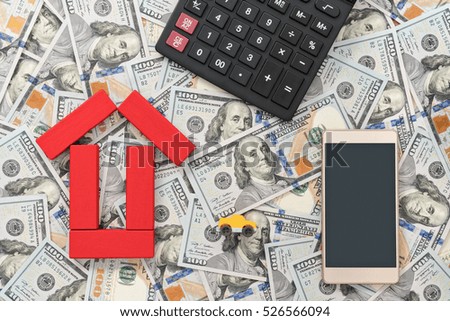 Smartphone, calculator, toy car and a house built of blocks laid out on a background of dollars, a top view