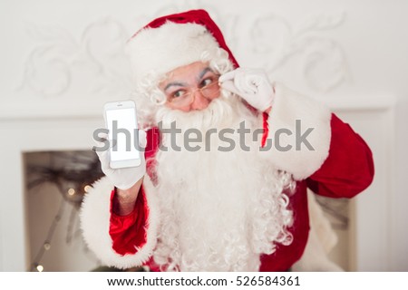 Santa Claus shows a smartphone with fireplace at background