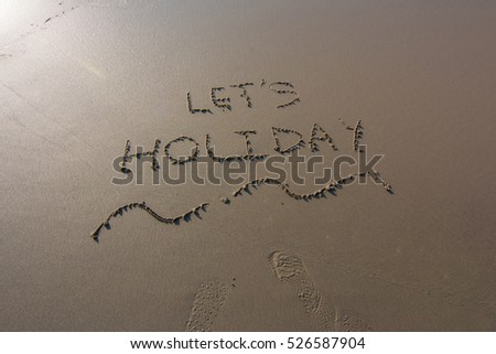 "Let's Holiday" written in the sand with a view of the ocean.Image has grain or blurry or noise and soft focus when view at full resolution