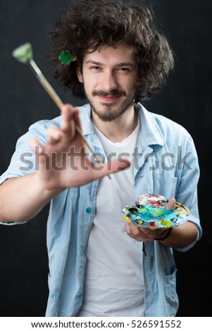 Portrait of an artist holding his brushe and paints. Shot in a studio.