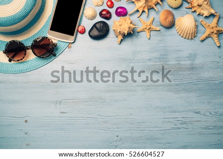 Straw hat sunglasses smartphone among sea shells and stones on wooden surface