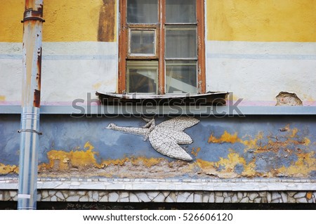 The window at the old, cracked wall, decorated with a mosaic picture of a man on a bird in one of St. Petersburg courtyards.