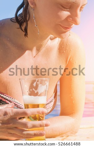 Handsome woman with glass of beer in the pool in the sunlight
