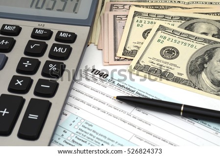 Financial IRS individual tax return 1040. Fill out the 1040 US individual tax return form. Black pen, american dollars heap, calculator. Tax Day and Tax Payment Concept. Royalty-Free Stock Photo #526824373