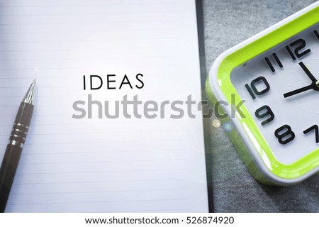 A word " IDEA " as a motivational quotes in the background of pen, book and green desk clock. Conceptual of business, education, finance, news.