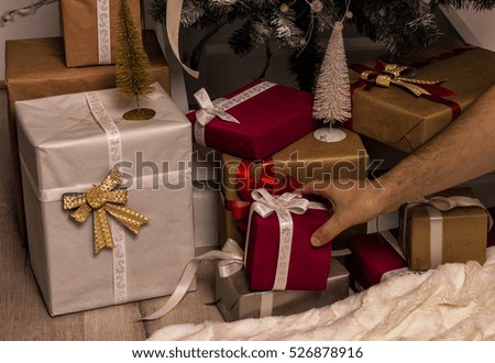 Hand of man putting or taking  Christmas gift . Decorated christmas tree and bunch of gifts on background