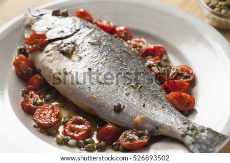 whole gilthead with cherry tomatoes and capers in the oven with chopped parsley and garlic sauce

