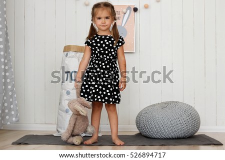 Mischievous girl standing on the carpet near the bag with toys in the nursery and holding toy hare in the hand, childhood and family concept, horizontal indoor portrait