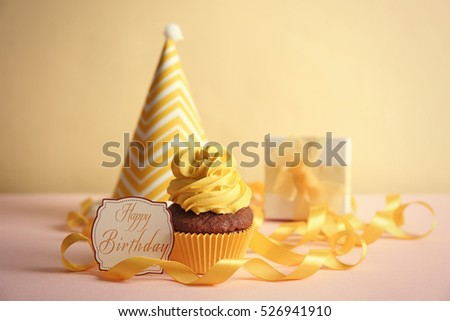 Delicious cupcake and greeting card on table. Text HAPPY BIRTHDAY on card.
