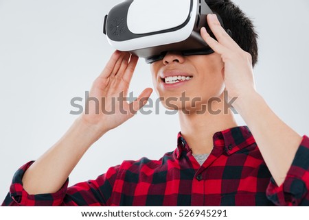 Picture of young asian man dressed in casual shirt in a cage and wearing virtual reality device. Isolated over white background.