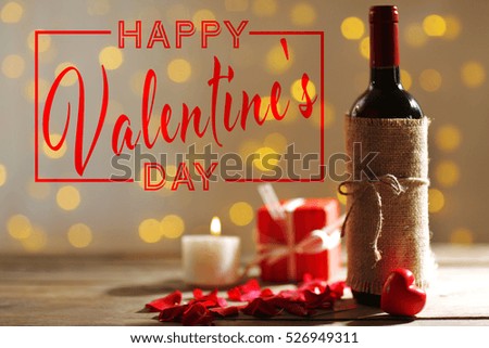 Text HAPPY VALENTINE'S DAY. Bottle of wine with flower petals on table.