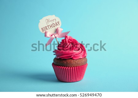 Delicious cupcake with greeting card on blue background. Text HAPPY BIRTHDAY on card.