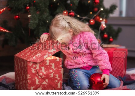 Adorable little girl opening a magical Christmas gift near a Christmas tree in cozy living room in winter. New year kid concept.