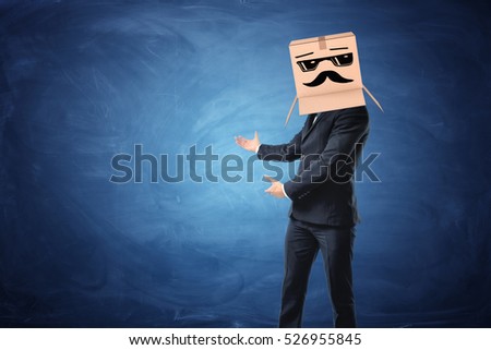 A businessman showing at something on the blue blackboard behind him, he is wearing a cardboard box with drawn sun glasses and moustache on his head. New opportunities. Interesting proposals