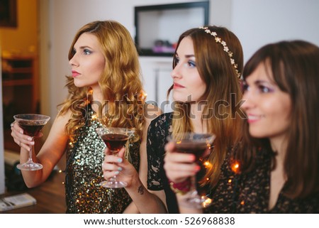 Three girls at a party with drinks in their hands, focus on the girl furthest from the camera.