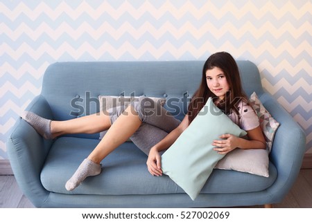 teen pretty girl with long dark hair lay on the sofa in pajamas with pillows