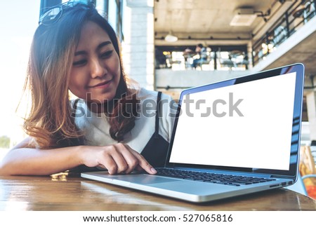 Mockup image of a woman using laptop and presenting with blank white screen on wooden table in modern cafe 