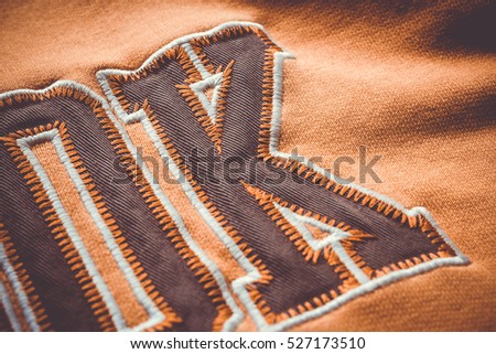Close-up to fabric of a orange blouse with a few letters saw on it