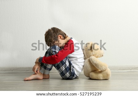 Sad little boy with teddy bear sitting on floor in empty room Royalty-Free Stock Photo #527195239