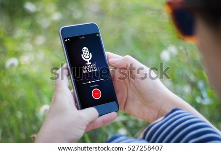 woman in the grass recording voice message. All screen graphics are made up. Royalty-Free Stock Photo #527258407