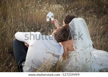 Newlywed couple holding a picture of a house