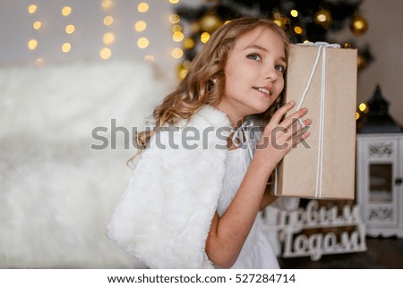 A girl in front of the fir-tree with a gift. New year's eve. Christmas eve. Cozy holiday at the fir-tree with lights and gold decor.