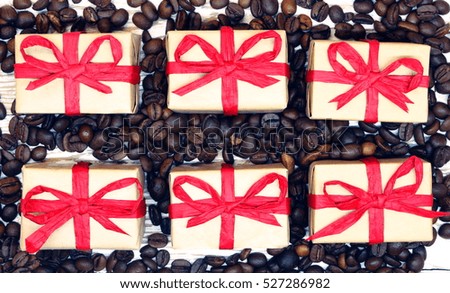 gift packages wrapped in gray paper with organic red ribbon, coffee beans on the wooden background; toned photo