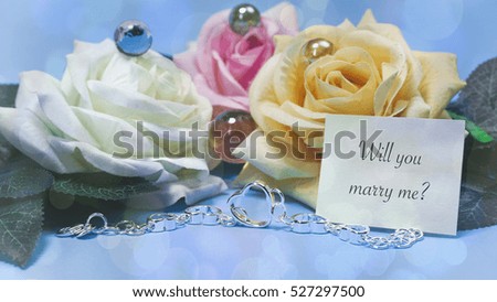 Roses and jewelry, blue background, words on paper will you marry me